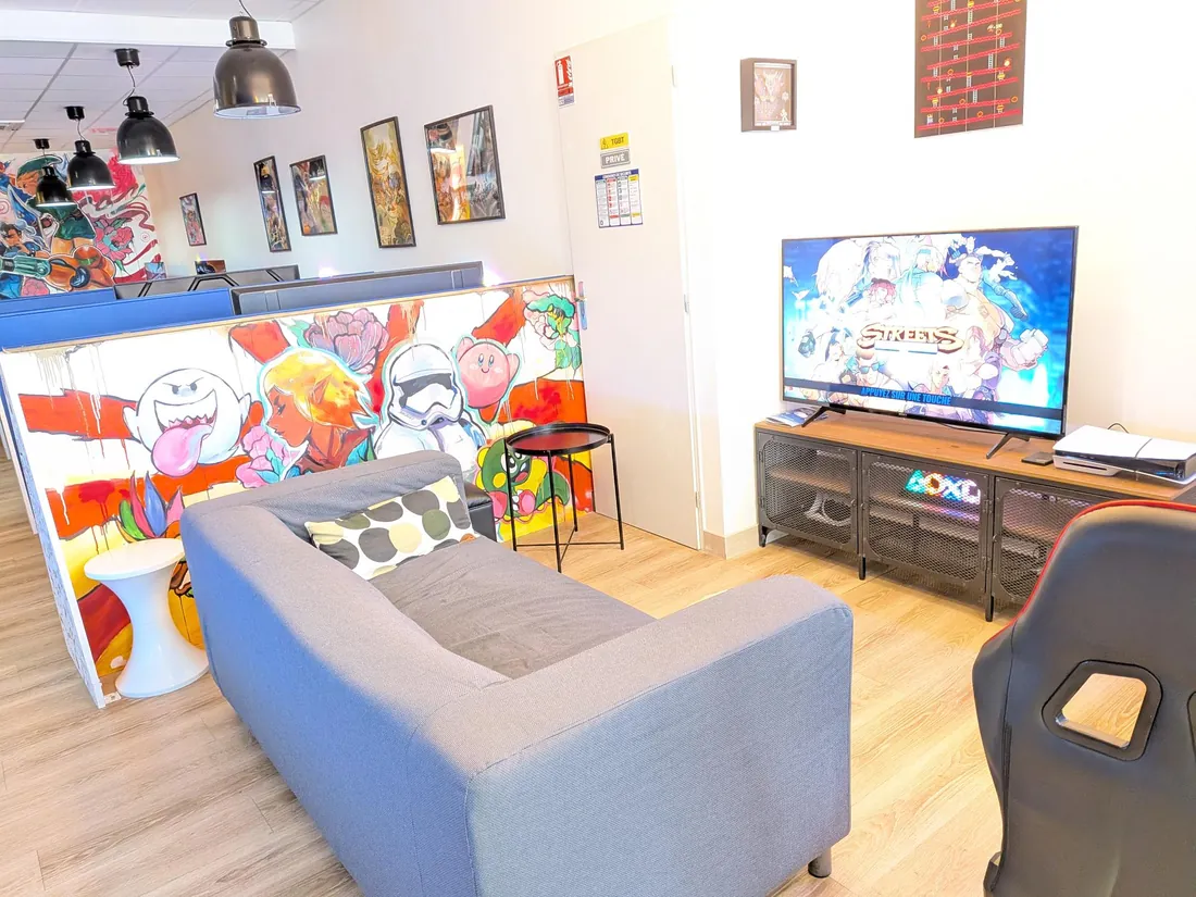 Alcôve de jeu avec canapé gris, grand écran et siège gamer